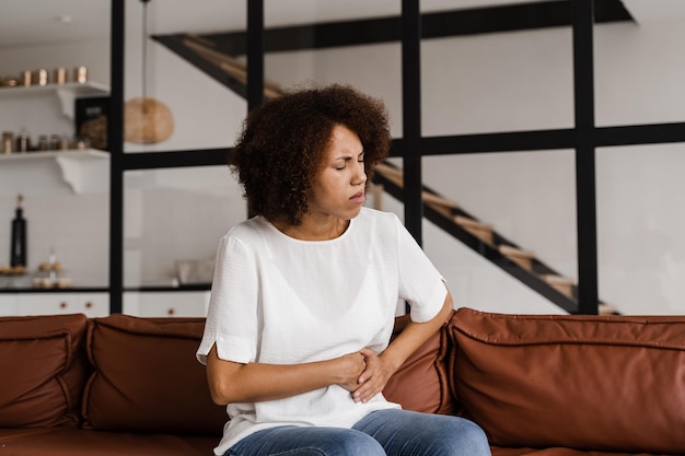 Photo douleurs à l'estomac une fille afro-américaine malade tient l'abdomen parce que ça fait mal la maladie de la pancréatite du pancréas s'enflamme