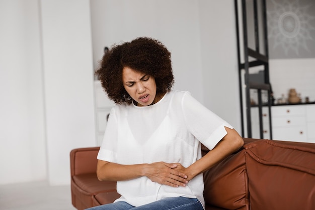 Douleurs à l'estomac La maladie de la pancréatite du pancréas s'enflamme Une fille afro-américaine malade tient l'abdomen parce que ça fait mal