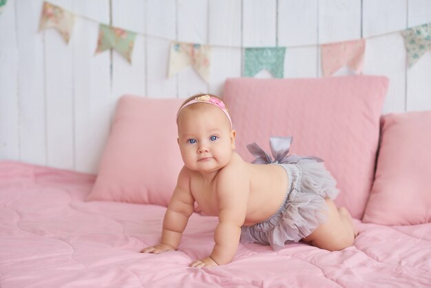 Doux bébé drôle sur le lit dans la chambre des enfants.Mignon bébé fille 6 mois assis et rampant.