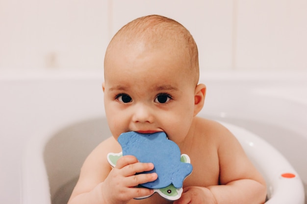 Doux bébé drôle prenant un bain. Bébé mâchant un jouet dans une chaise de bain. Baignade en toute sécurité.