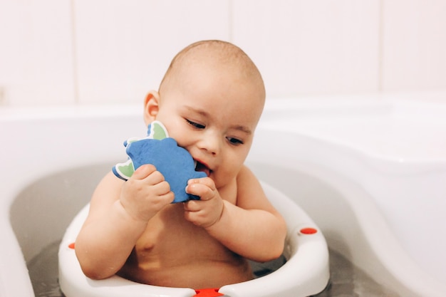 Doux bébé drôle prenant un bain. Bébé mâchant un jouet dans une chaise de bain. Baignade en toute sécurité.