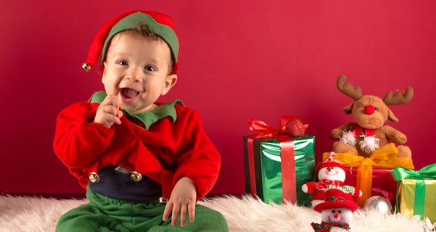 Doux garçon d'un an habillé comme un elfe en décoration de Noël avec des cadeaux