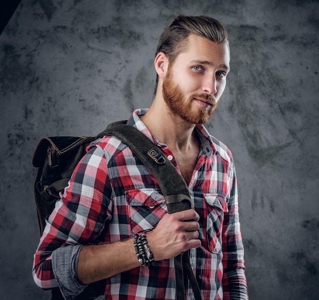 Doux mâle roux barbu dans une chemise avec un sac de voyage sur son épaule.