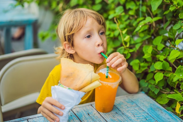 Doux petit garçon caucasien mangeant des crêpes et buvant du jus d'orange