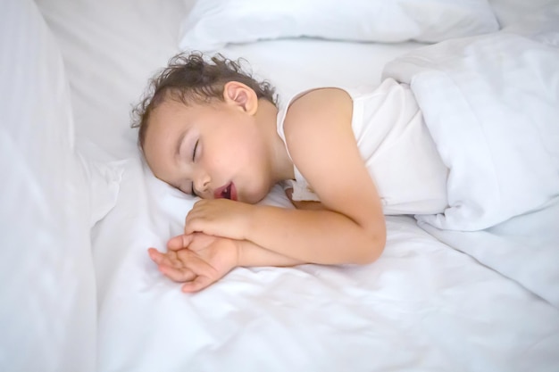 Doux petit garçon dort sur un lit blanc