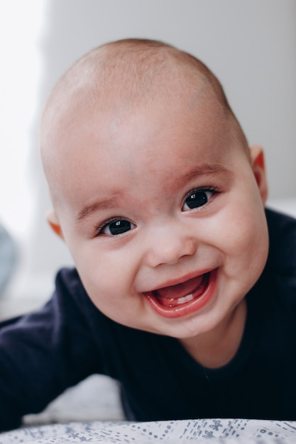 Photo doux petit garçon effronté joufflu allongé sur le ventre sur le lit. expression de visage drôle.