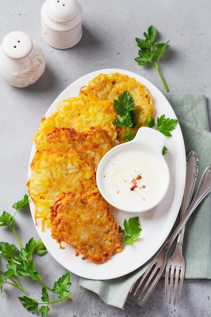 Draniki - ritters de pommes de terre, crêpes de pommes de terre végétariennes, servies avec des herbes fraîches et sauce au yogourt à l'ail sur une vieille table. vue de dessus.