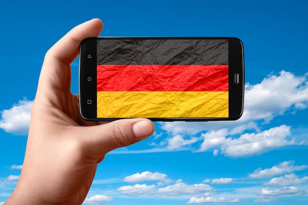 Drapeau de l'Allemagne sur l'écran du téléphone Smartphone à la main montre un drapeau sur un fond de ciel avec des nuages Photographie mobile