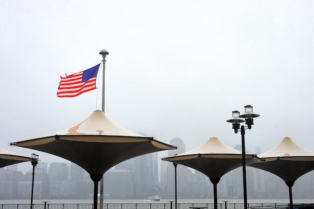 Photo drapeau américain en lambeaux qui souffle dans le vent avec les toits de manhattan sur fond un jour de pluie