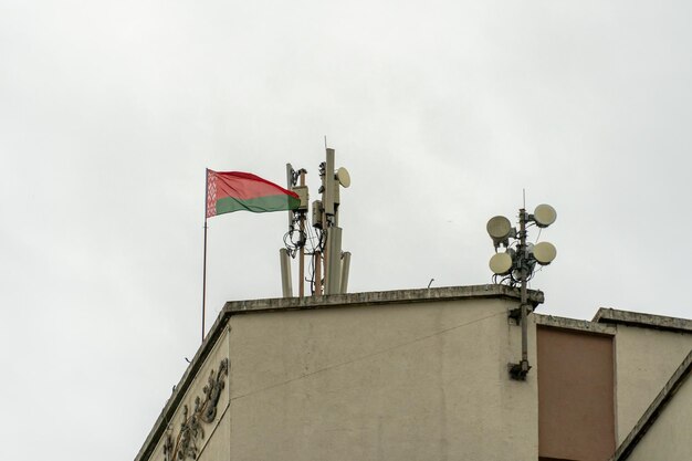 Photo le drapeau de la biélorussie est installé sur le toit du bâtiment près de la nouvelle antenne gsm pour transmettre le signal 5g pollution radioactive de l'environnement par les tours cellulaires
