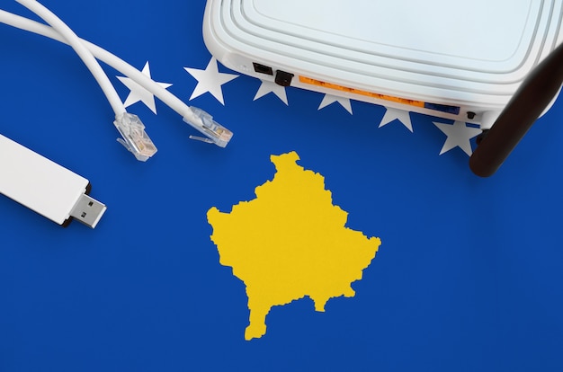 Drapeau du Kosovo représenté sur une table avec un câble Internet RJ45, un adaptateur WiFi USB sans fil et un routeur. Concept de connexion Internet