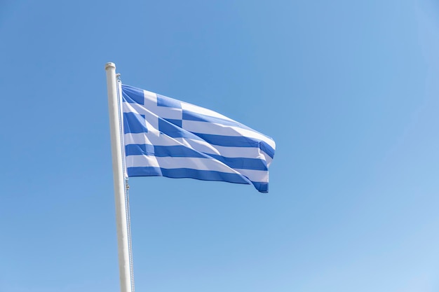 Le drapeau de la Grèce agite dans le ciel bleu clair. fond