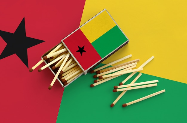 Le drapeau de la Guinée-Bissau est représenté sur une boîte d'allumettes ouverte, à partir de laquelle plusieurs matches tombent et repose sur un grand drapeau