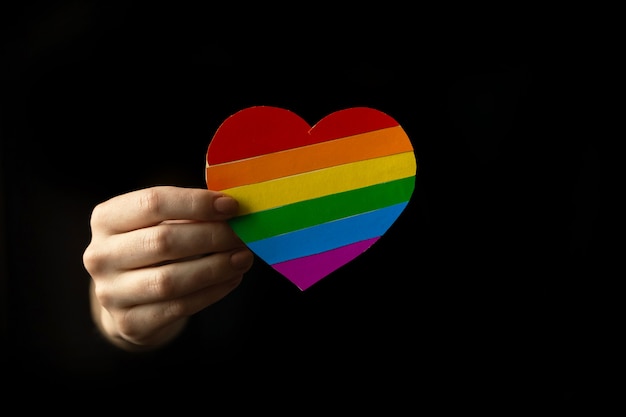 Drapeau LGBT, main avec coeur aux couleurs de l'arc-en-ciel, symbole de l'amour. Photo de fond noir