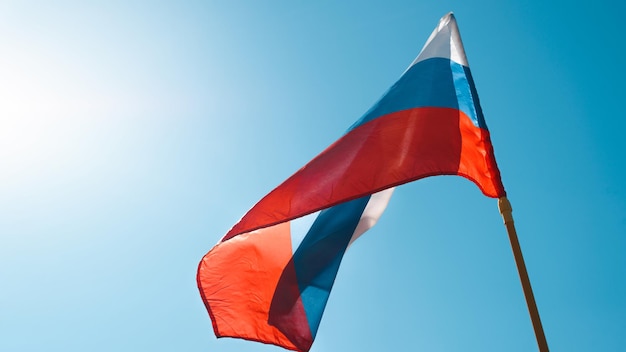 Drapeau national tricolore de la Fédération de Russie agitant dans le vent contre un ciel bleu clair par une journée ensoleillée à l'extérieur