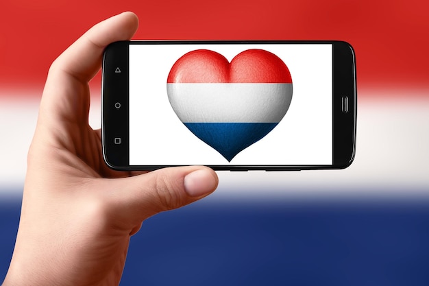 Drapeau néerlandais en forme de coeur sur l'écran du téléphone Smartphone à la main montre un drapeau coeur