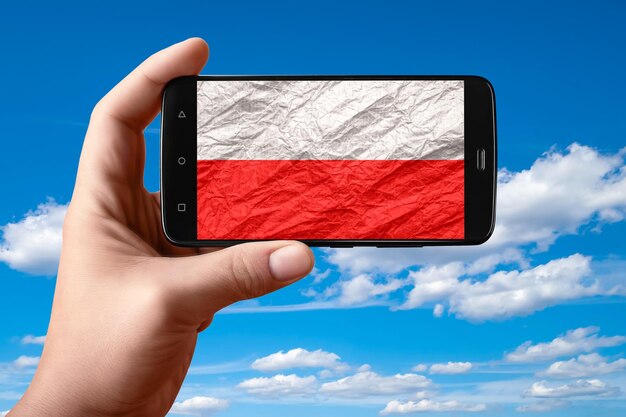 Drapeau polonais sur l'écran du téléphone Smartphone à la main montre un drapeau sur un fond de ciel avec des nuages Photographie mobile