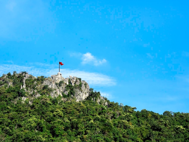 Drapeau rouge sur l'immense sommet de la montagne verte sur fond de ciel bleu avec espace de copie. Concept de réussite, de victoire, de leadership et de réalisation des objectifs.