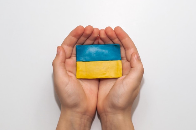 Le drapeau de l'Ukraine fait de pâte à modeler dans les mains d'un enfant sur fond blanc