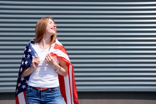 Photo drapeau usa étoiles et rayures. fille de gingembre élégant joyeux avec des lèvres peintes en rouge et les yeux fermés debout avec le drapeau des états-unis