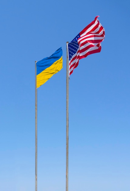 Les drapeaux des États-Unis et de l'Ukraine volent au vent contre le ciel bleu