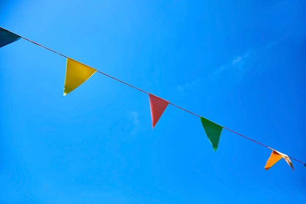 Drapeaux de festival en papier triangulaire multicolore sur fond de ciel bleu Ambiance festive de fête en plein air