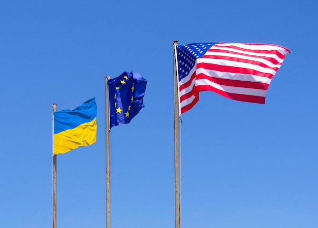 Les drapeaux des États-Unis, de l'Union européenne et de l'Ukraine volent au vent contre le ciel bleu