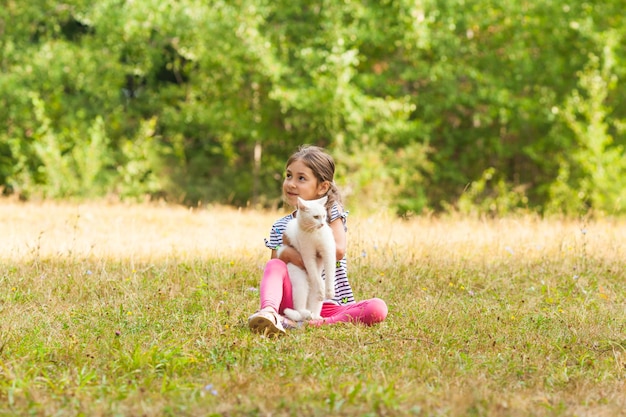 Dreamingfull fille de six ans assise sur une herbe embrassant son chat blanc moelleux sur un fond de parc de la ville de la forêt verte