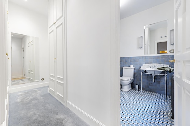 Un dressing avec un miroir au mur moquette gris pâle et accès à une salle de bain avec des meubles vintage dans les tons bleus