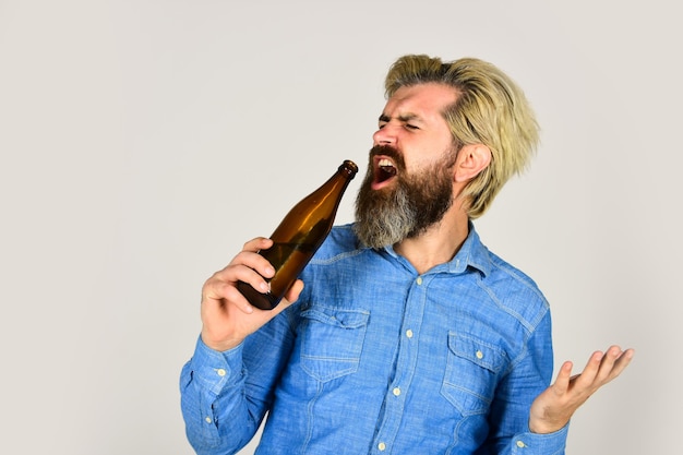 Drôle de chanteur de bière et de football se détendre après une journée de travail permet de s'amuser un homme barbu a la gueule de bois un homme mûr boit de la bière de l'eau saine dans une bouteille en verre un hipster brutal qui boit de l'alcool