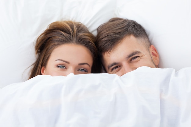 Drôle de couple amoureux allongé dans le lit se cachant sous une couverture