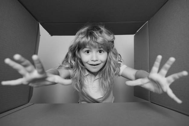 Drôle d'enfant garçon ouvre un cadeau et regarde à l'intérieur d'une boîte en carton enfant avec une boîte ouverte à prendre à la main gi