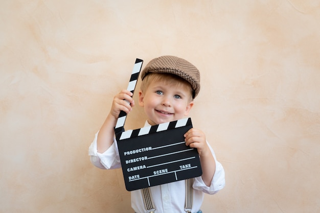 Drôle enfant tenant clap. Heureux enfant s'amusant à la maison. Concept de cinéma rétro