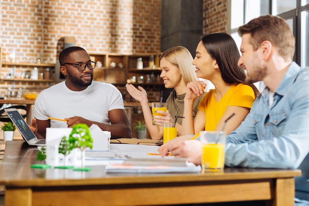 Drôle d'étude. Quatre étudiants énergiques et créatifs assis à la table tout en parlant et en planifiant la stratégie