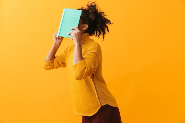 Photo drôle de femme africaine portant un chandail tenant un livre sur son visage isolé