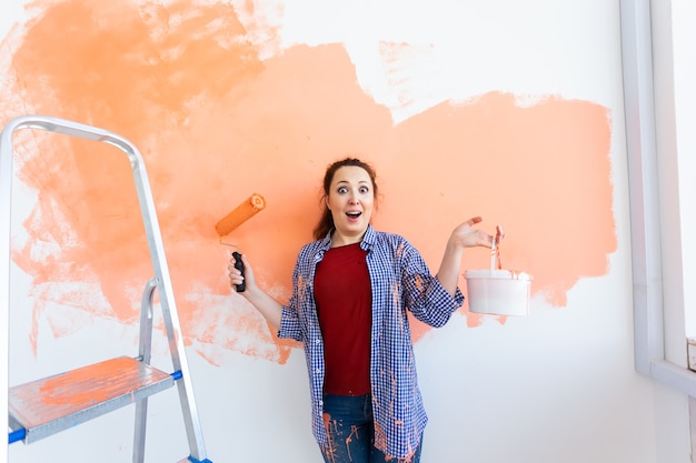 Drôle femme souriante peinture mur intérieur de la maison avec rouleau à peinture. Redécoration, rénovation