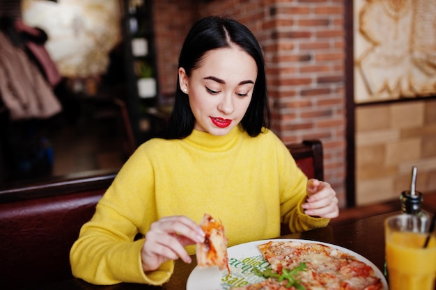 Drôle de fille brune en pull jaune, manger de la pizza au restaurant