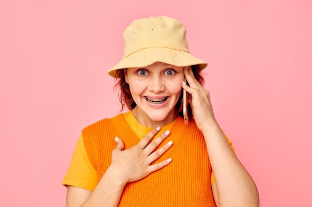 Drôle de fille avec un téléphone à la main boucles d'oreilles grimace cap fashion fond rose inchangé