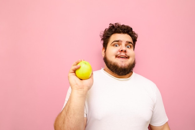 Drôle de gars en surpoids en t-shirt blanc isolé sur fond rose avec une pomme verte