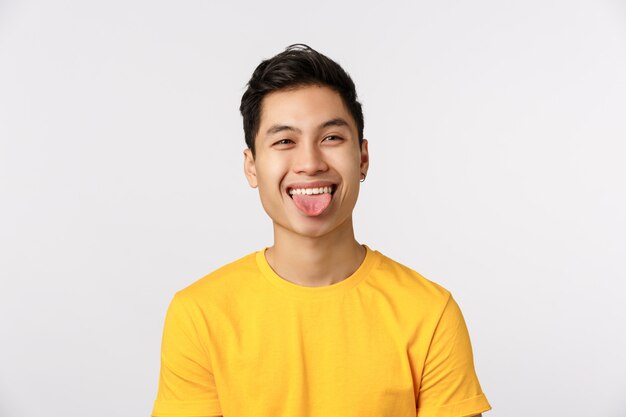 Drôle homme asiatique mignon en t-shirt jaune montrant la langue