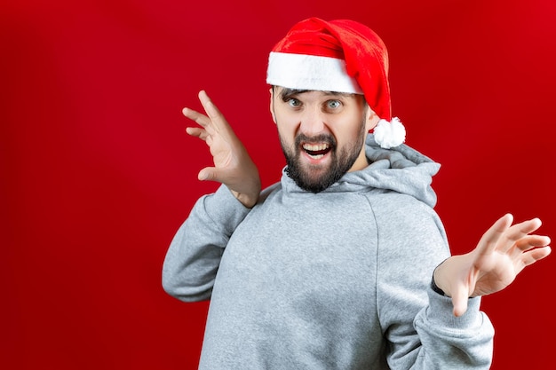 Un drôle d'homme barbu dans un chapeau de père Noël rouge avec un stabilisateur dans ses mains grimace devant l'appareil photo du smartphone