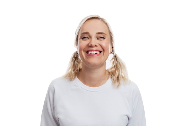 Drôle de jeune femme blonde en riant dans un pull blanc. Isolé sur un mur blanc.