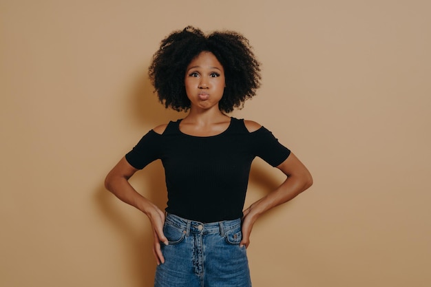 Photo drôle jeune femme à la peau foncée insouciante gonflant ses joues sur fond de mur de studio nu