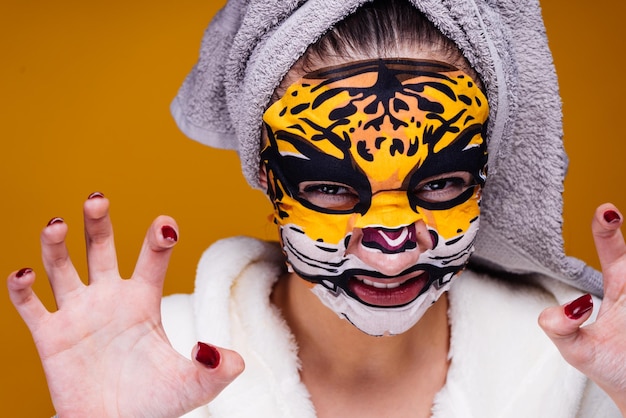 Une drôle de jeune fille avec une serviette sur la tête grogne comme une bête sur son visage un masque hydratant avec un visage de léopard