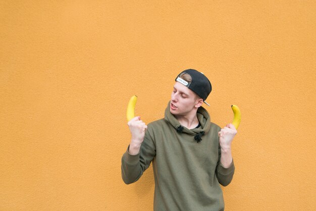 Un drôle de jeune homme debout sur un mur orange avec des bananes dans ses mains. Un regard sur les bananes