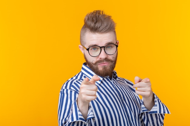 Drôle de jeune homme avec une moustache et une barbe sans chemise et lunettes montre sur un mur jaune