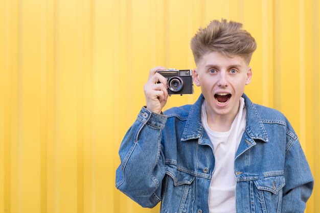 Drôle jeune homme photographiant un appareil photo rétro et regardant la caméra.