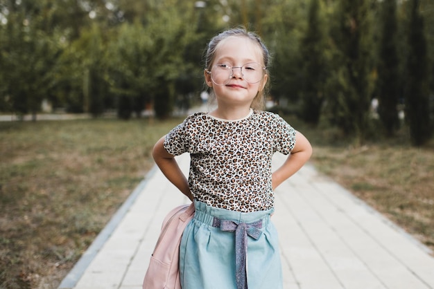 Drôle mignon enfant fille 4-5 ans porter des lunettes et des vêtements décontractés tenant un sac à dos dans le parc