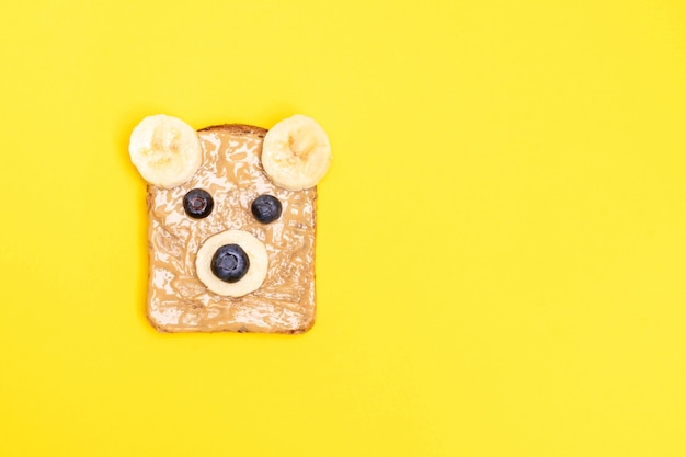 Drôle de petit-déjeuner pour enfants avec du beurre d'arachide en forme d'ours à la myrtille et à la banane. Vue de dessus, espace copie