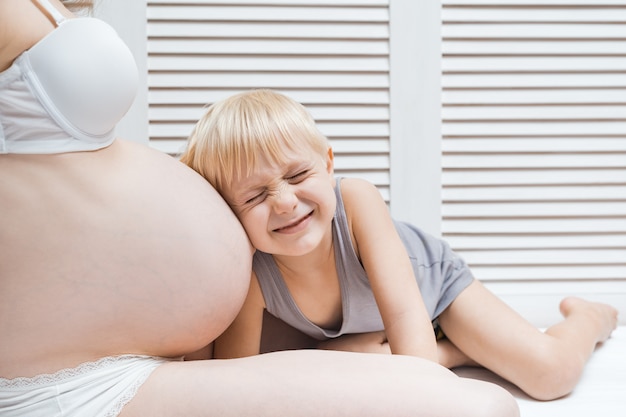 Un drôle de petit garçon appuya son oreille sur le ventre de sa mère enceinte, ferma les yeux et écouta. Deuxième concept de grossesse